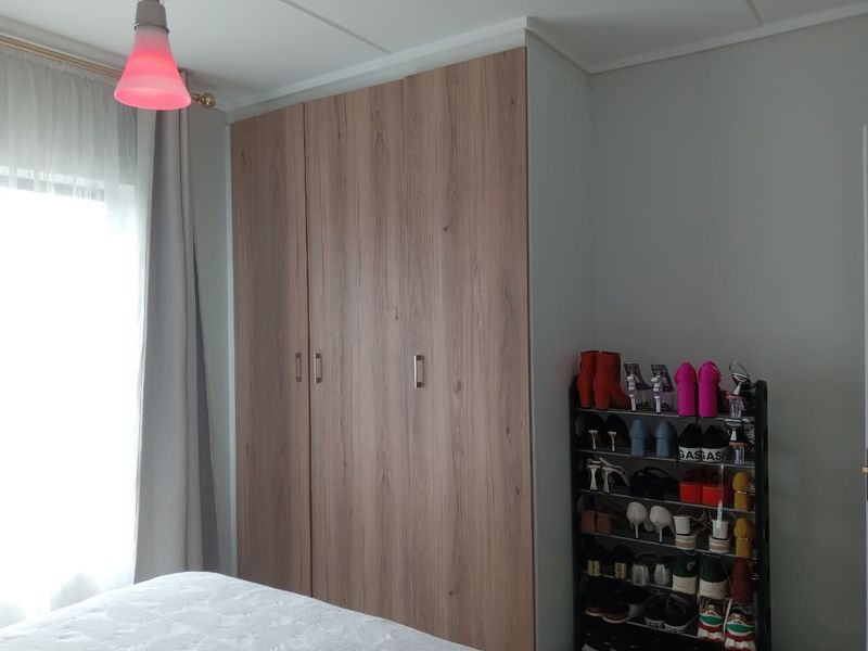 A bedroom featuring a modern wood-finish built-in wardrobe with ample storage space.