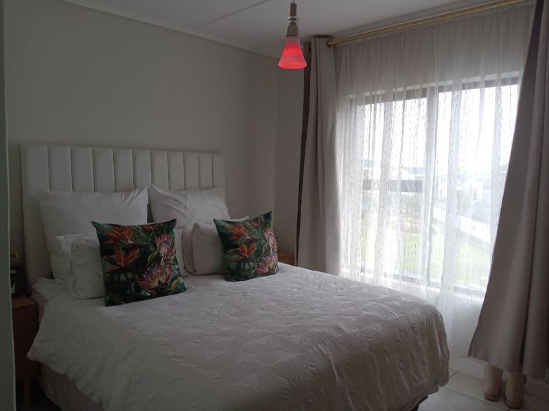 A well-lit bedroom featuring a large window with curtain tracks and a modern pendant light fixture.