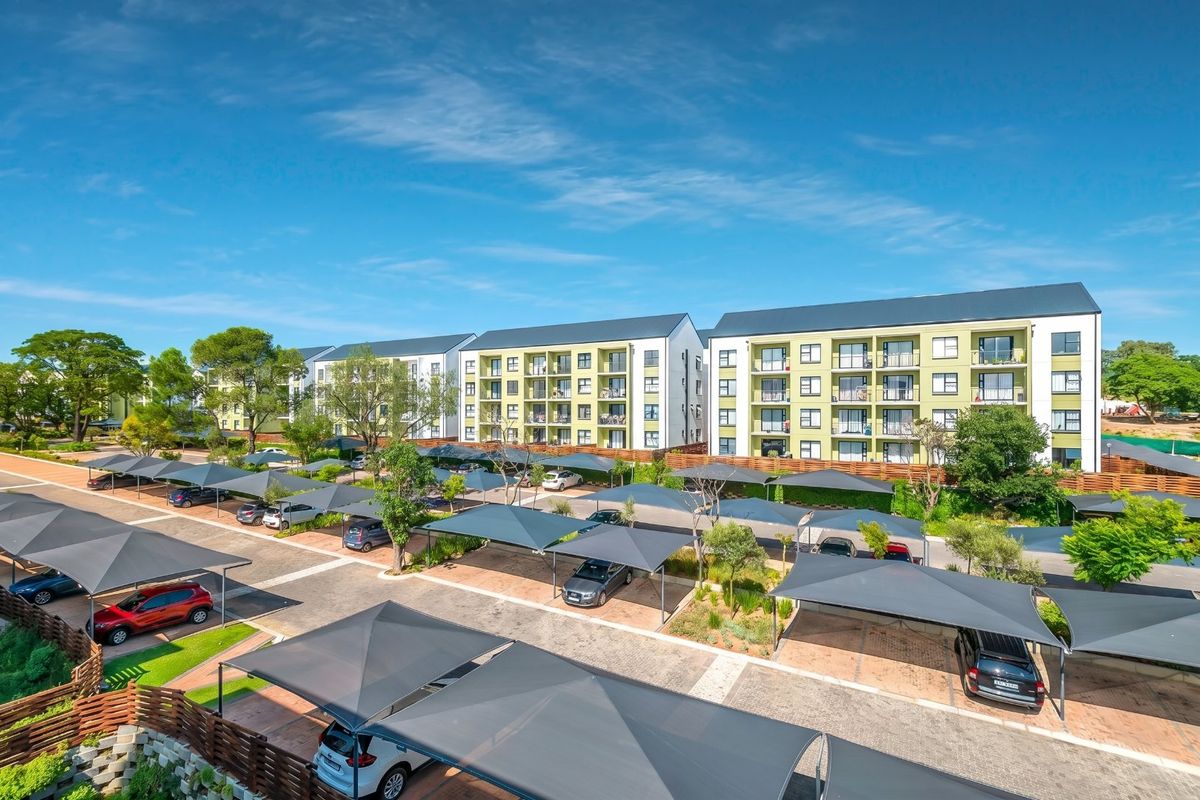 Aerial view of a modern apartment complex featuring multiple residential blocks, paved parking areas with shade cloth carports, and landscaped grounds.