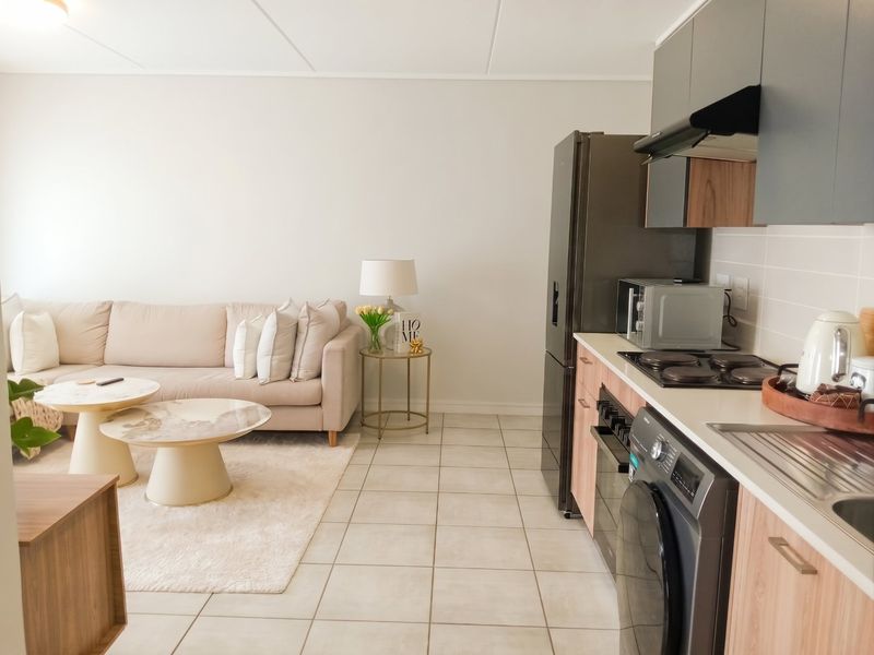 An open-plan living area featuring a modern kitchen with built-in cabinetry, integrated appliances, and tiled flooring, seamlessly connected to the living space.