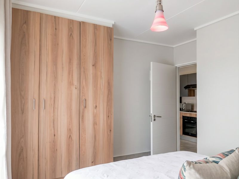 A well-maintained bedroom featuring modern wood-finish built-in wardrobes and a clean, neutral aesthetic with direct access to the kitchen area.