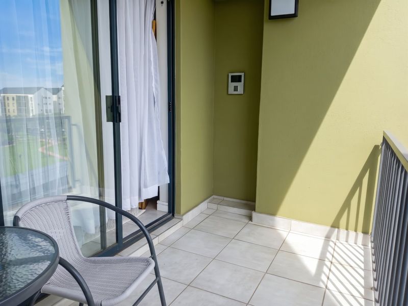 A clean, tiled balcony featuring a sliding glass door, metal railing, and an intercom system, offering a functional outdoor space.