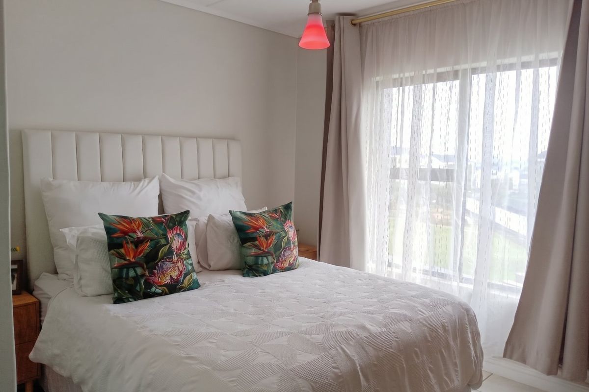 A well-maintained bedroom featuring a large sliding window with sheer curtains and a modern pendant light fixture.