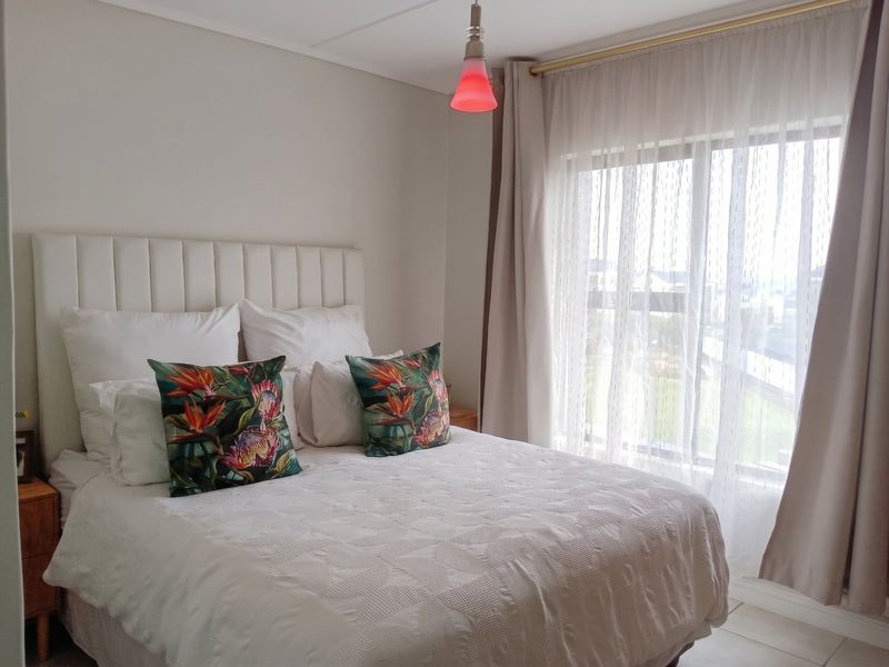 A well-maintained bedroom featuring a large sliding window with sheer curtains and a modern pendant light fixture.