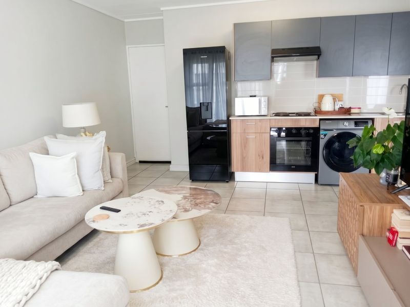 Modern open-plan living area featuring a compact kitchen with built-in cabinetry, integrated appliances, and neutral tiled flooring throughout.