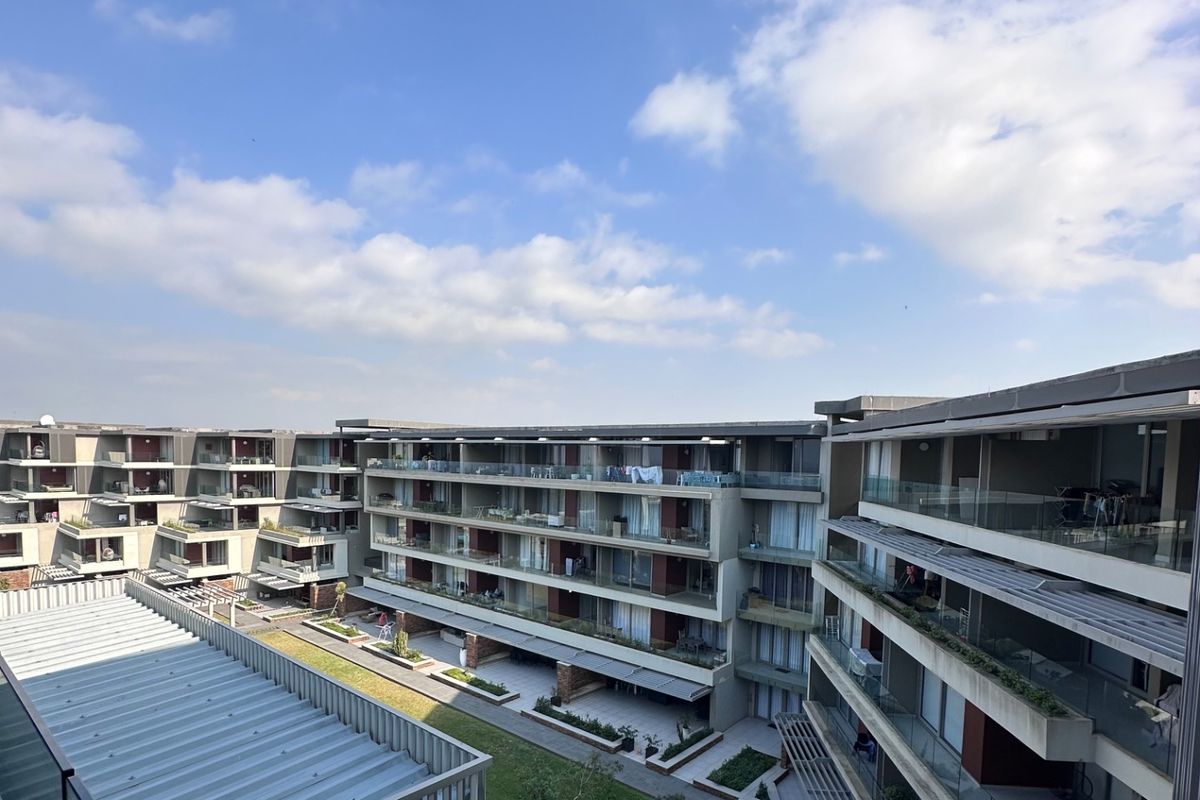 An elevated view of a modern apartment complex featuring multiple levels of balconies with glass railings and a central landscaped courtyard area.
