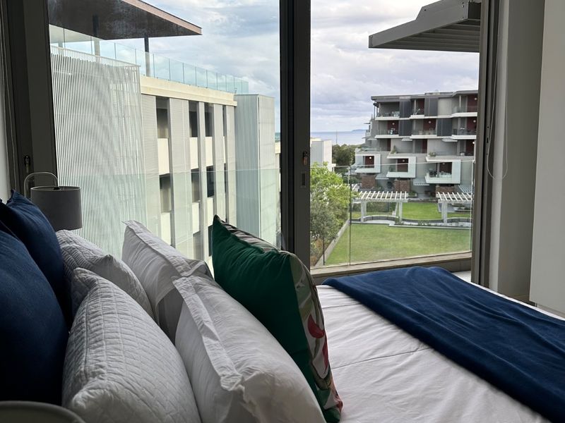 Bedroom featuring large sliding glass doors that open to a balcony with views of the surrounding apartment complex and distant sea.