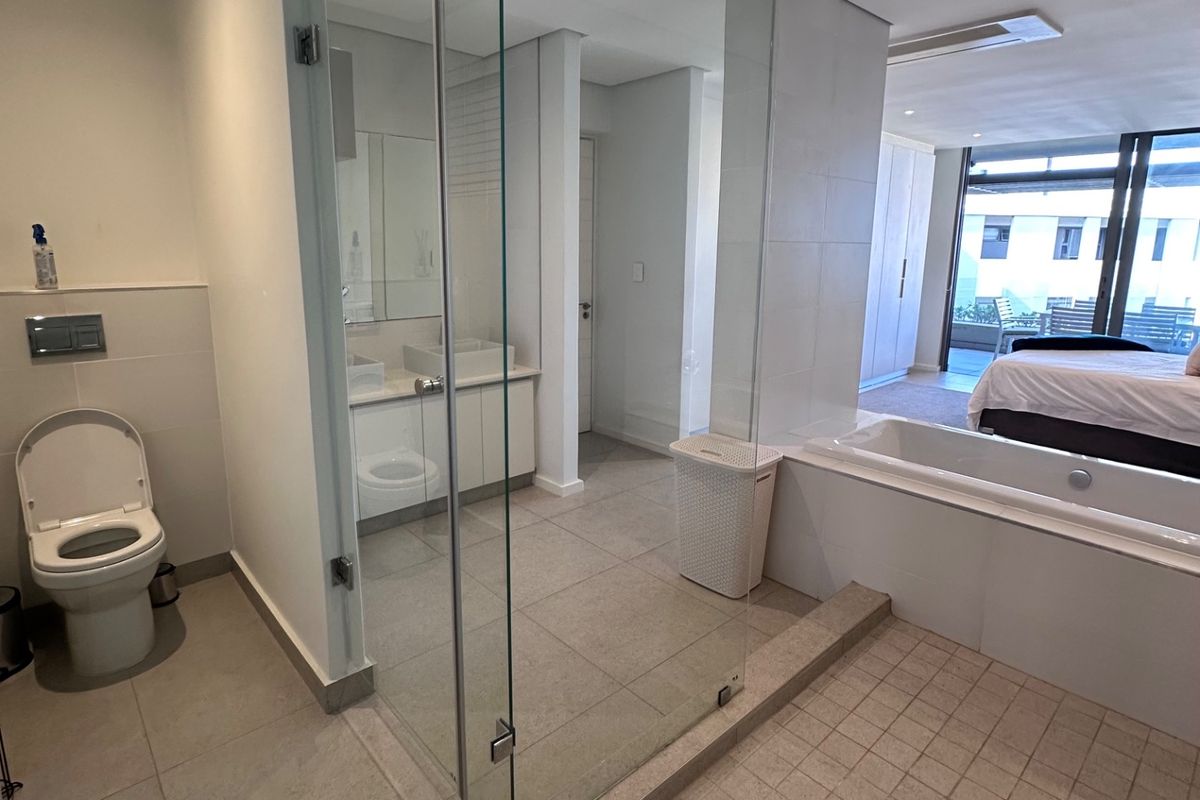 Modern open-plan bathroom featuring a glass-enclosed shower, built-in bathtub, dual vanity, and wall-mounted toilet with neutral tiled finishes.