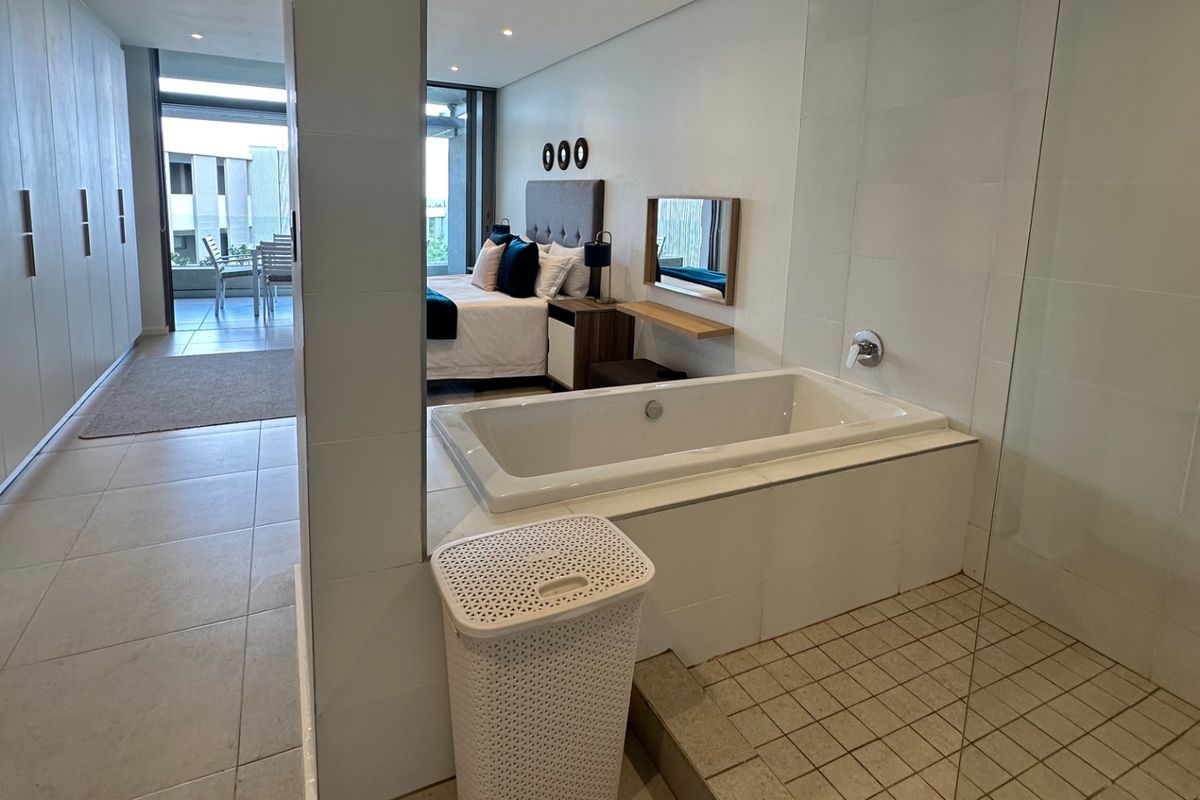 Open-plan bedroom suite featuring a built-in bathtub, tiled flooring, ample cupboard space, and direct access to a private balcony.