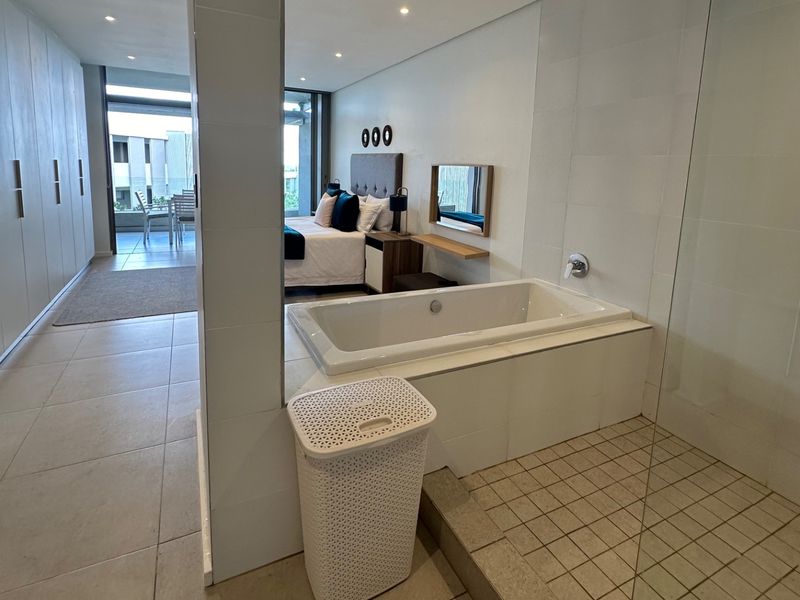 Open-plan bedroom suite featuring a built-in bathtub, tiled flooring, ample cupboard space, and direct access to a private balcony.