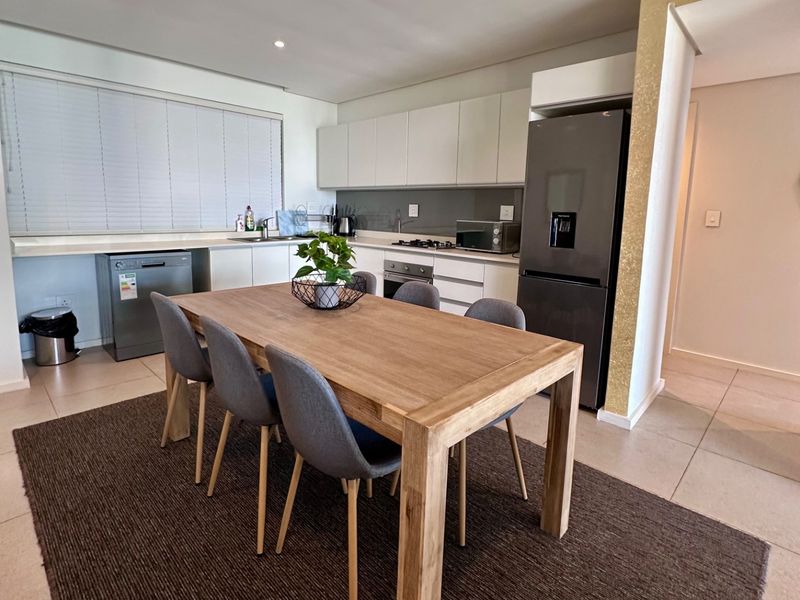 Modern open-plan kitchen and dining area featuring sleek white cabinetry, integrated appliances, and neutral tiled flooring, creating a bright and functional living space.