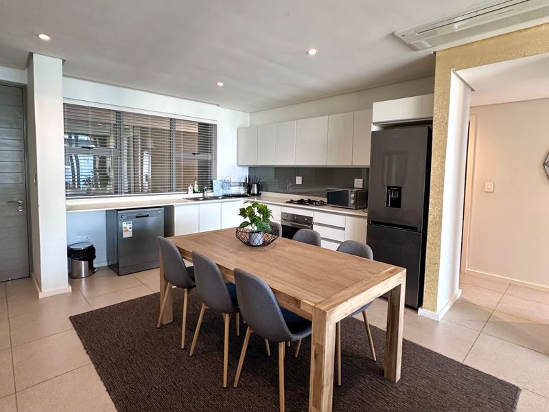 Modern open-plan kitchen and dining area featuring sleek cabinetry, integrated appliances, tiled flooring, and recessed lighting, creating a functional and contemporary living space.