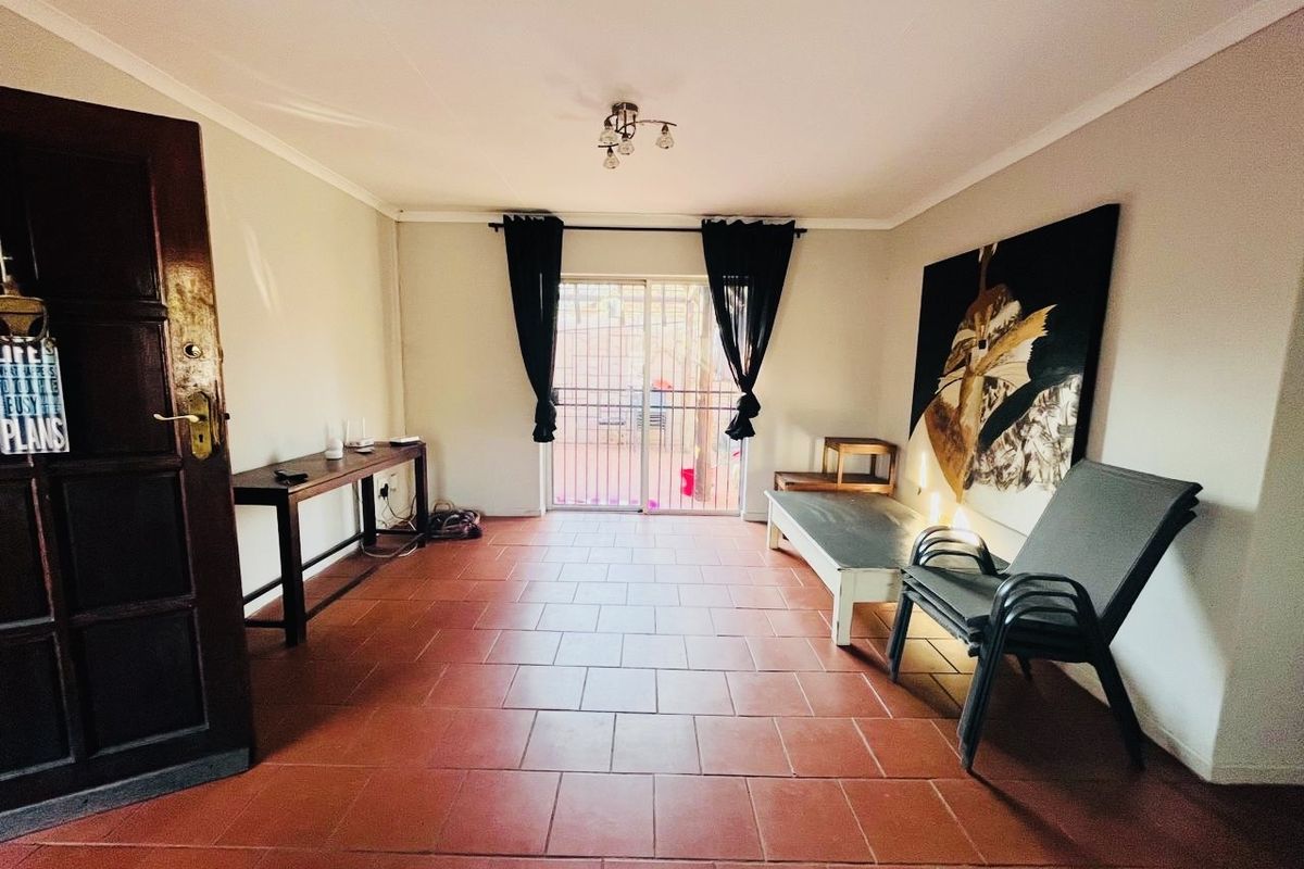 A living room featuring terracotta floor tiles and a sliding glass door with a security gate, providing access to the exterior.