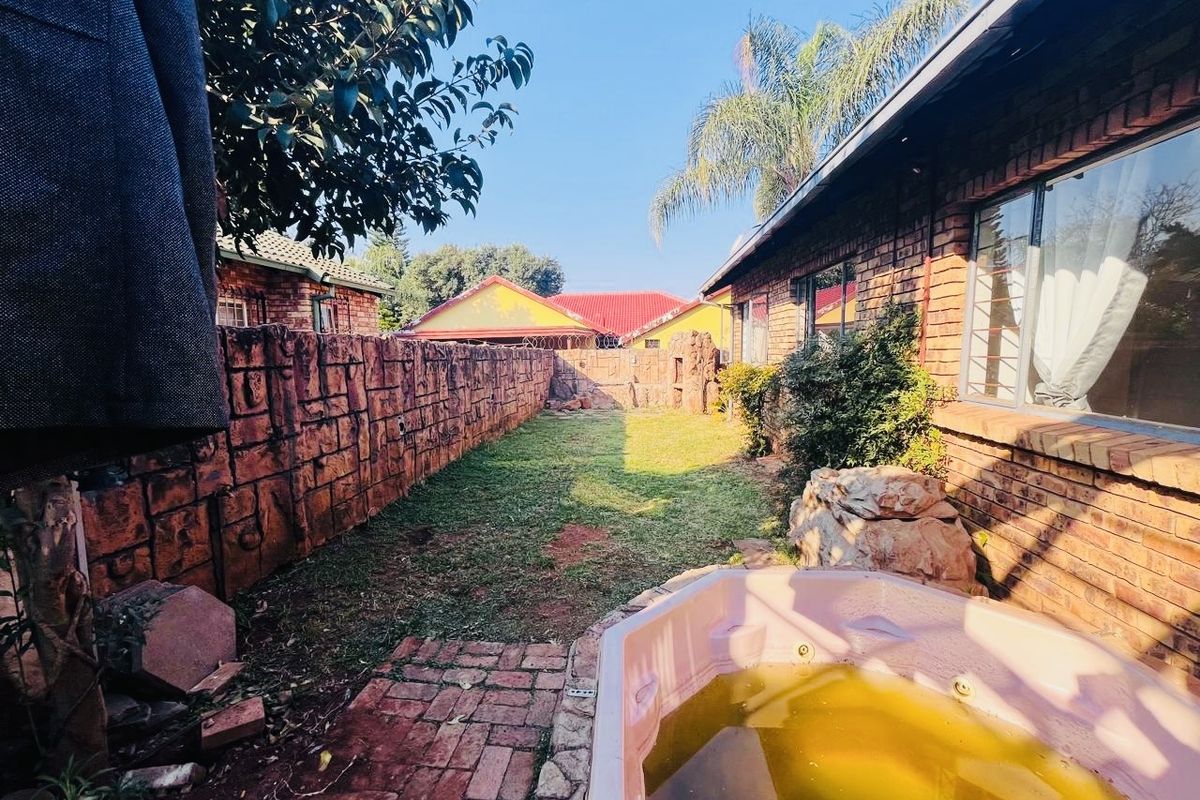 Rear garden area featuring a face brick exterior, paved walkway, and a built-in spa requiring maintenance.