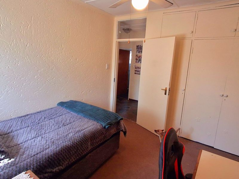 A bedroom featuring built-in cupboards, a ceiling fan, and a transom window above the doorway, with carpet flooring and textured wall finishes.