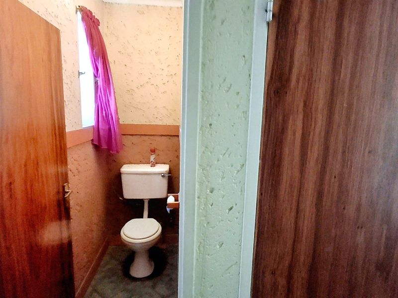 A small, dated bathroom featuring a standard toilet and textured wall finishes, requiring cosmetic updates to modernize the space.