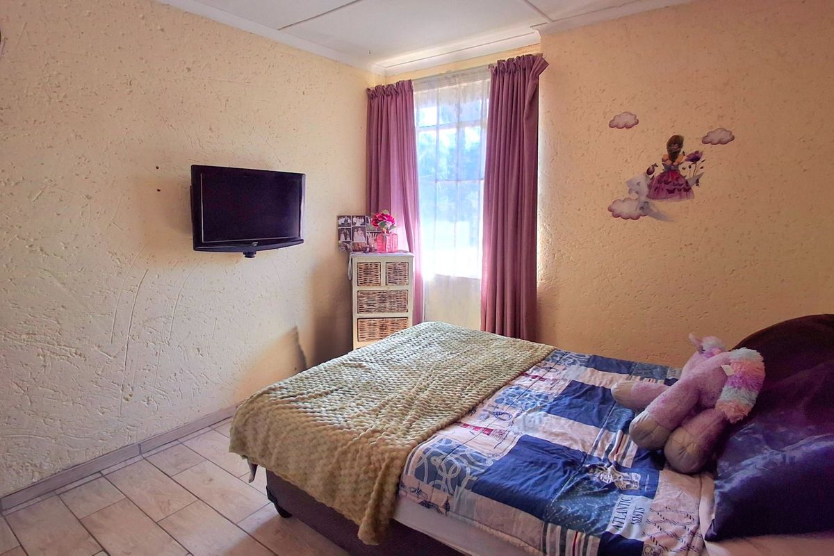 A functional bedroom featuring tiled flooring, textured walls, and a wall-mounted television bracket, offering a comfortable space with natural light.