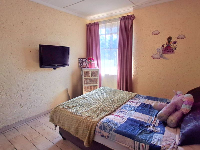 A functional bedroom featuring tiled flooring, textured walls, and a wall-mounted television bracket, offering a comfortable space with natural light.