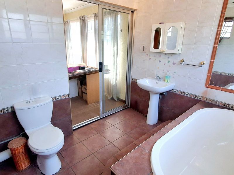 A functional bathroom featuring a pedestal basin, built-in bathtub, and ceramic tiling, with a sliding glass door leading to an adjacent room.