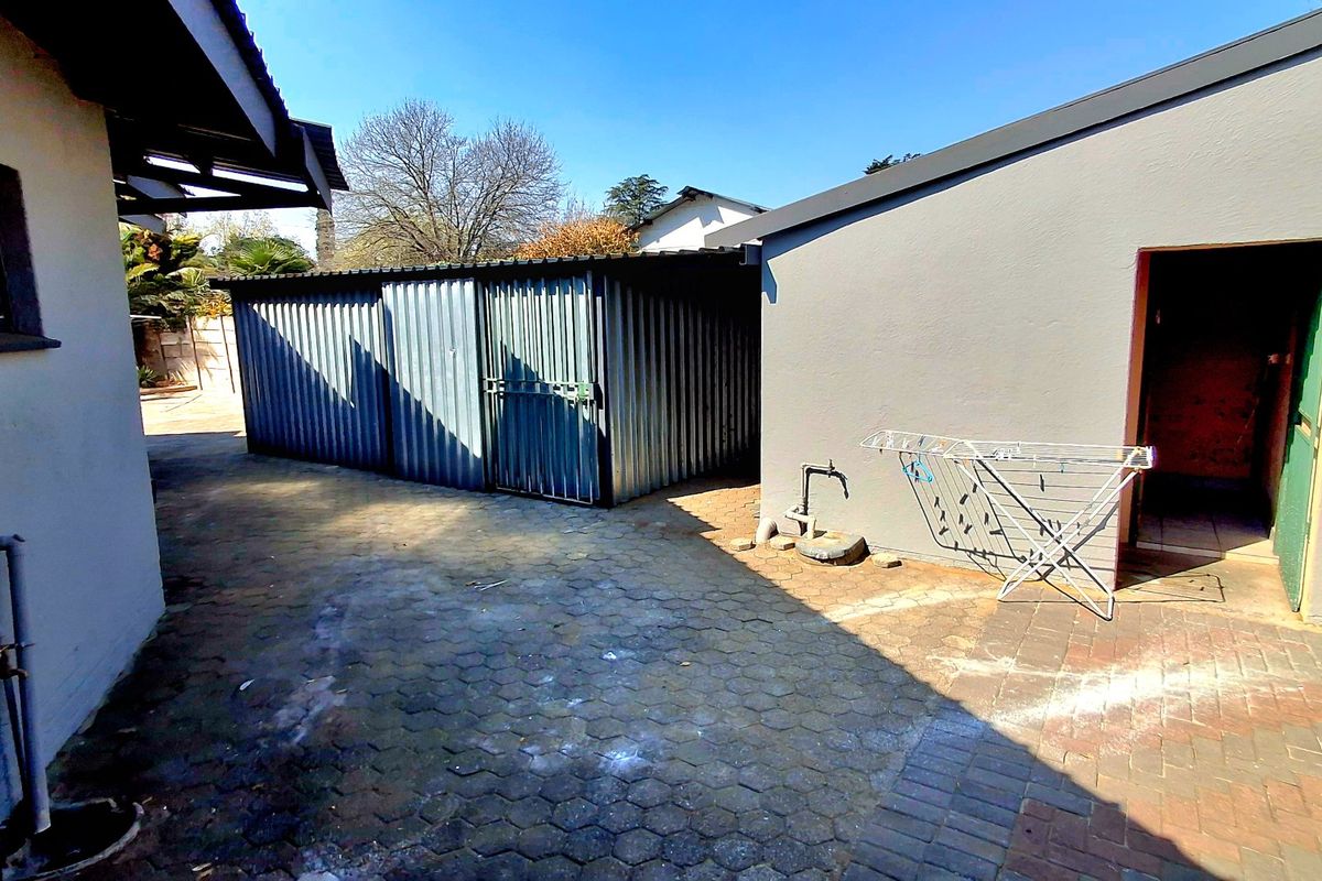 Rear exterior area featuring a paved courtyard, corrugated metal storage shed, and external utility access.
