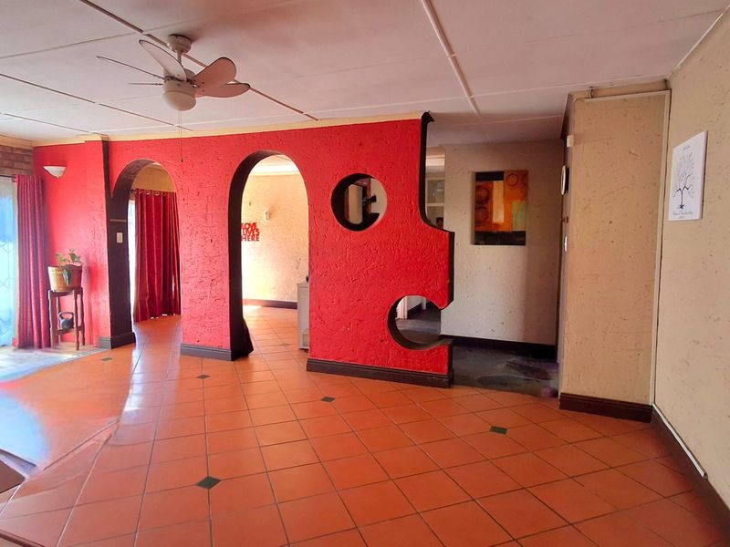 Spacious living area featuring distinctive red arched room dividers, tiled flooring, and a ceiling fan, offering a unique layout with potential for modernization.