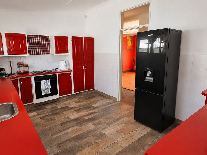 A functional kitchen featuring red cabinetry, laminate countertops, a built-in oven with gas hob, and tiled flooring.