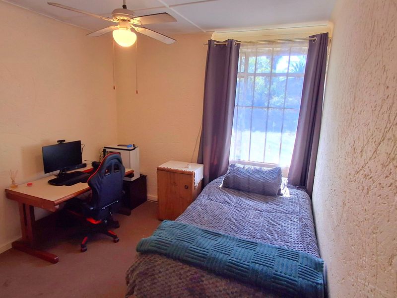A compact bedroom featuring a textured wall finish, a ceiling fan, and a window providing natural light.