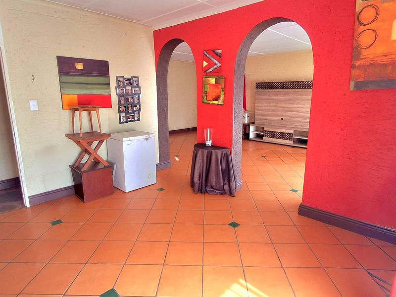 Living area featuring distinctive arched doorways, terracotta-style floor tiles, and bold red accent walls, offering a unique layout with potential for modernization.