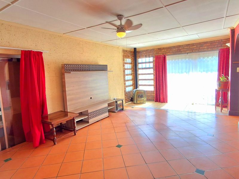 Spacious living room featuring tiled flooring, an exposed brick feature wall, a freestanding fireplace, and a ceiling fan, with direct access to the outdoor area.