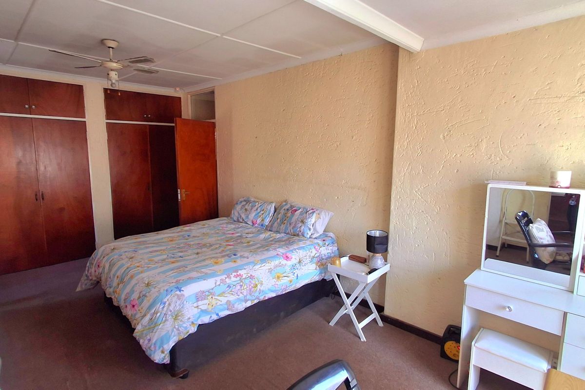 Spacious bedroom featuring built-in wooden cupboards, a ceiling fan, and carpeted flooring, offering a functional layout with potential for cosmetic updates.