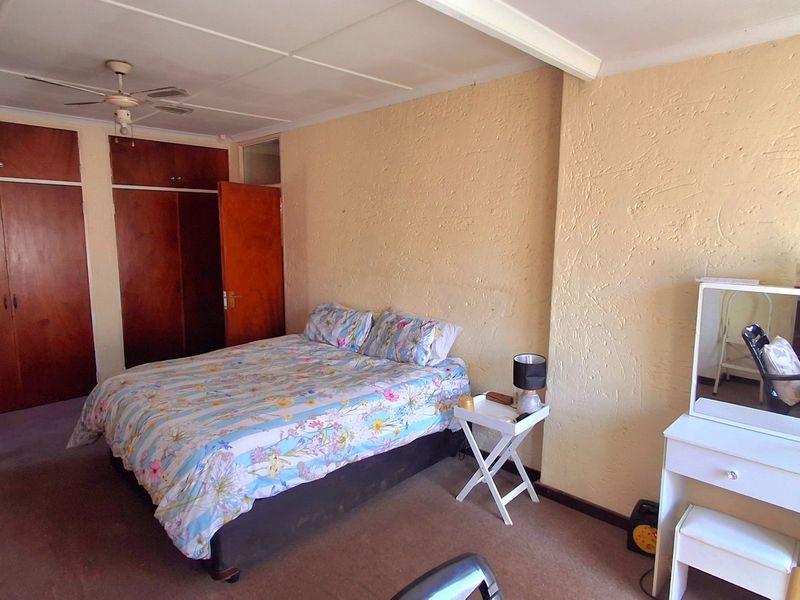 Spacious bedroom featuring built-in wooden cupboards, a ceiling fan, and carpeted flooring, offering a functional layout with potential for cosmetic updates.
