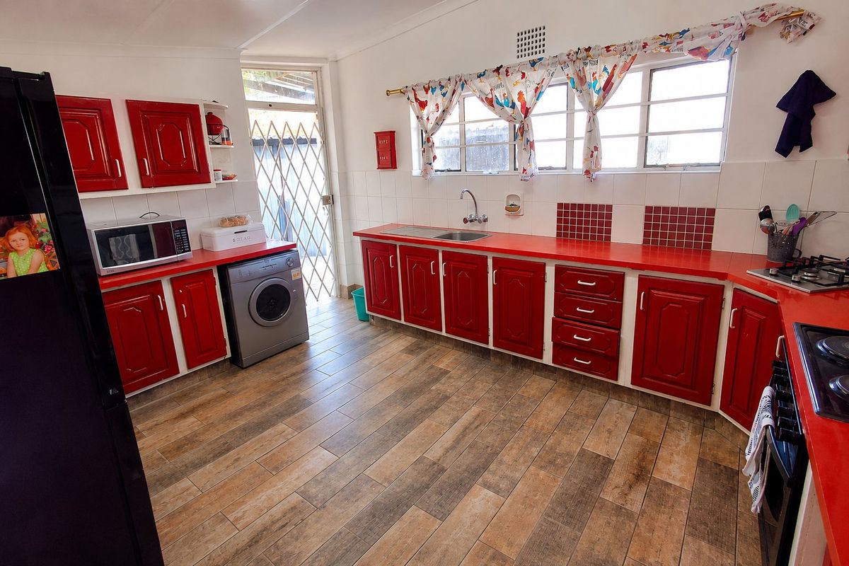 A functional kitchen featuring red cabinetry, laminate countertops, tiled backsplash, and integrated cooking appliances with direct access to the exterior.