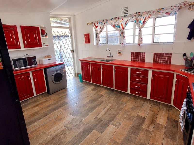 A functional kitchen featuring red cabinetry, laminate countertops, tiled backsplash, and integrated cooking appliances with direct access to the exterior.