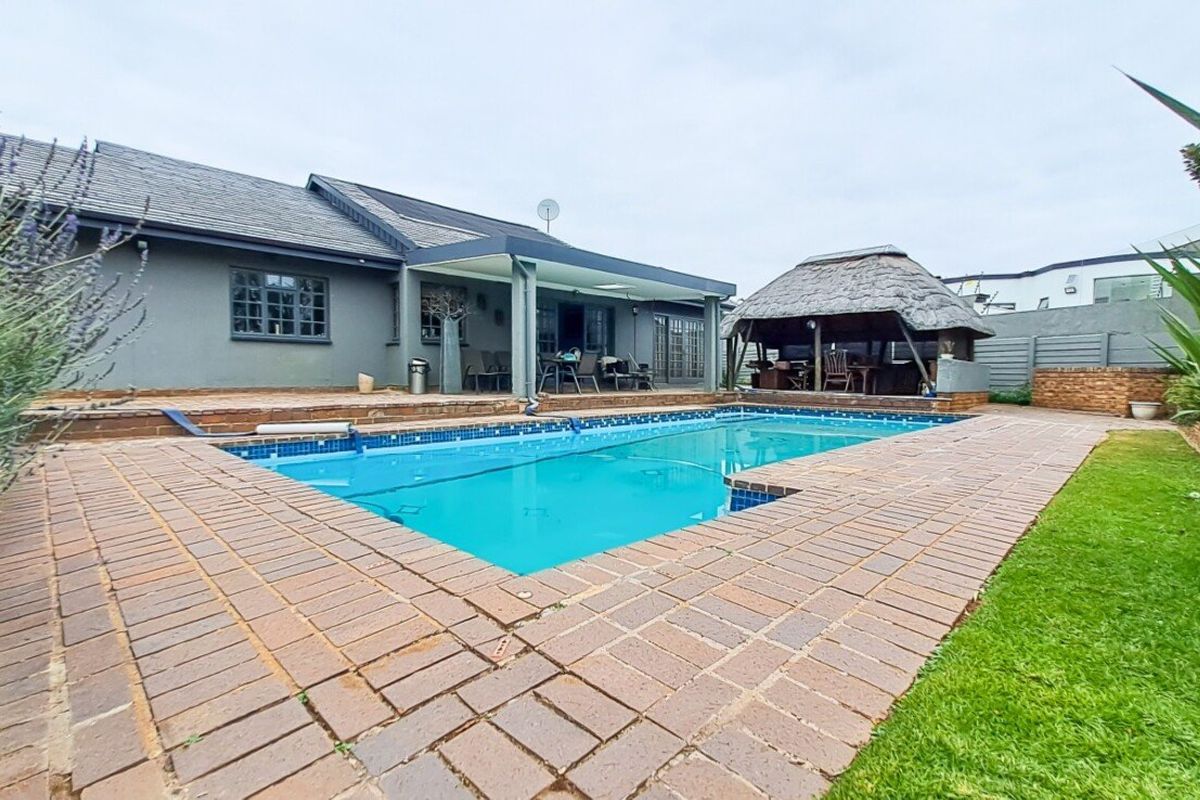 Outdoor entertainment area featuring a swimming pool, brick-paved surround, and a traditional thatched lapa, set against the rear elevation of the house.