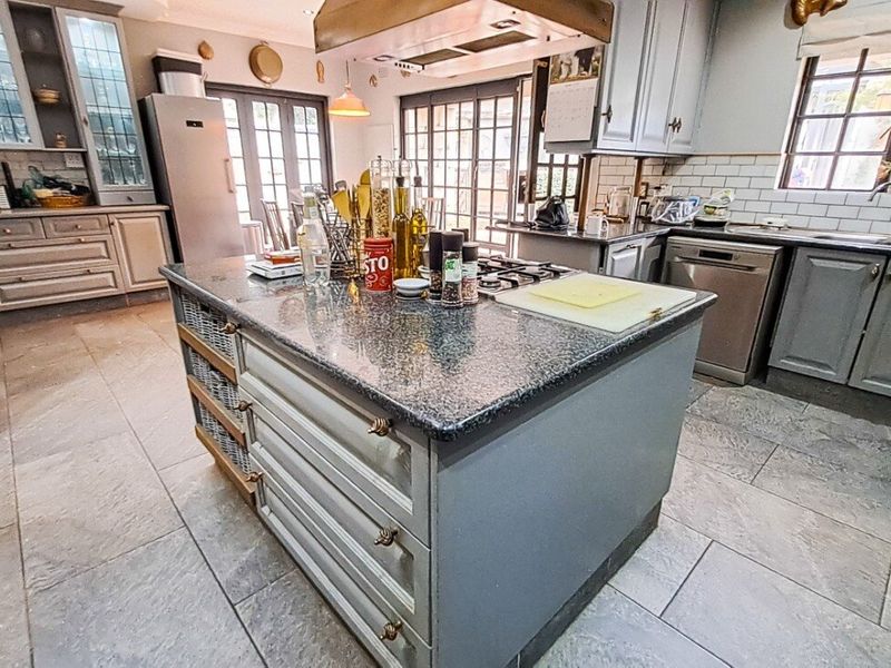 Spacious kitchen featuring a central island with granite countertops, gas hob, extractor fan, and ample built-in cabinetry with a classic design.