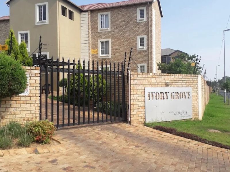 Front entrance view of Ivory Grove apartment complex featuring a paved driveway, secure metal gate, and facebrick building facade with electric fencing.