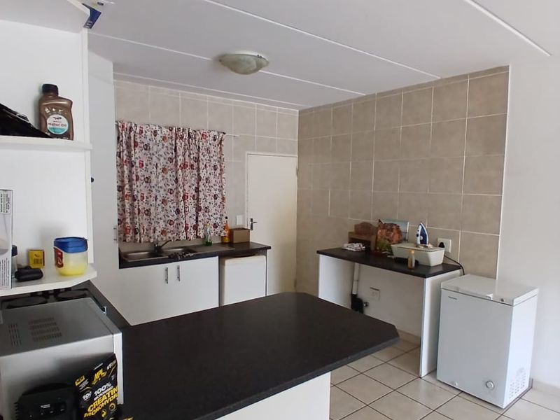 Functional kitchen area featuring tiled flooring, neutral wall tiles, built-in cabinetry, and laminate countertops with a breakfast bar extension.