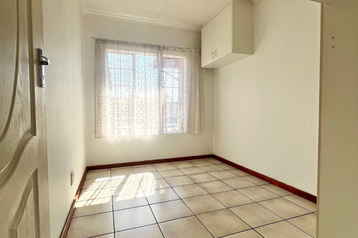 A bright, empty bedroom featuring neutral tiled flooring, a built-in overhead storage cupboard, and natural light from the window.