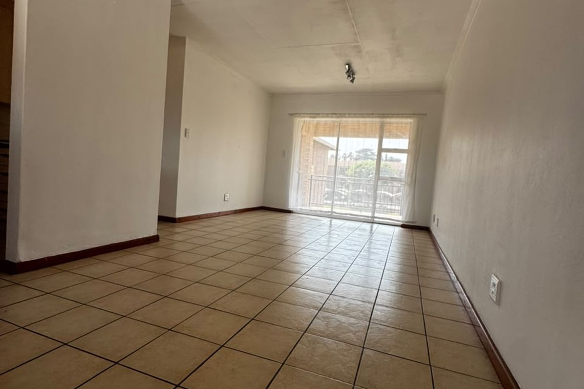 An empty, open-plan living area featuring tiled flooring and a sliding glass door leading to a balcony, with visible ceiling damage.