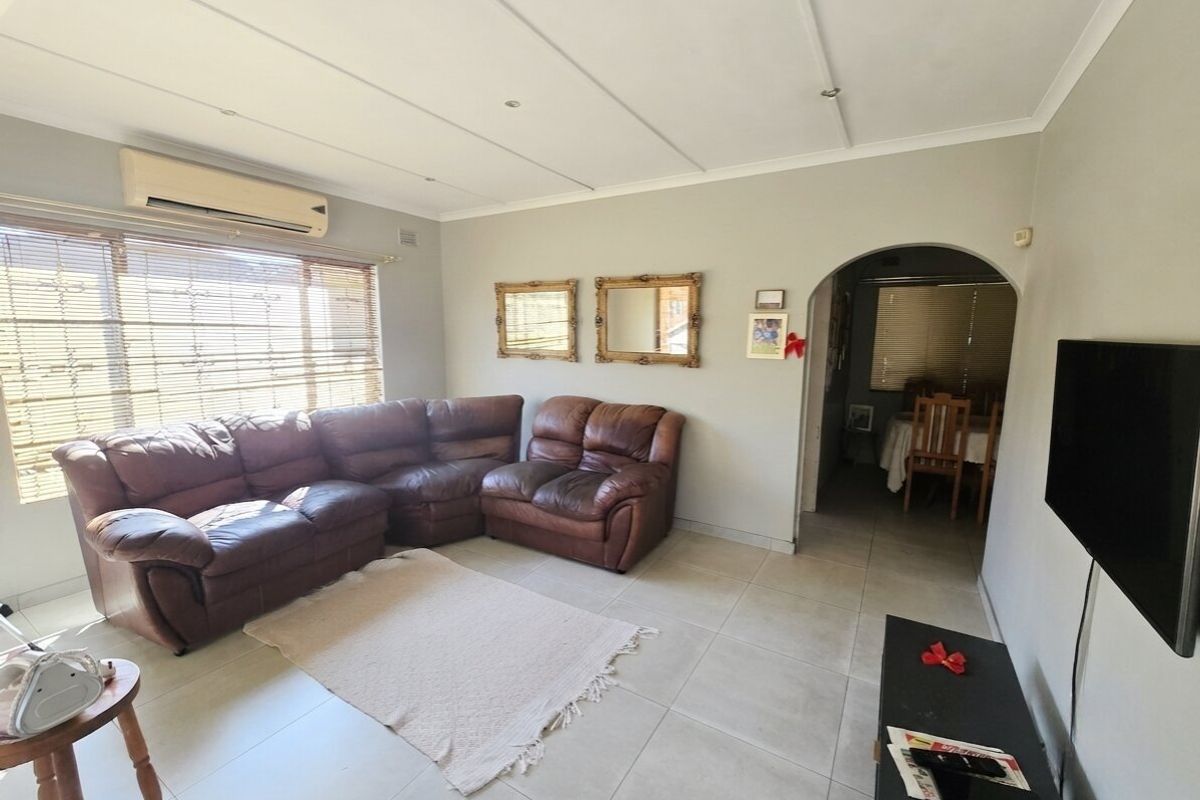 A comfortable living room featuring tiled flooring, a split-system air conditioner, and an arched entryway leading to the adjacent dining area.