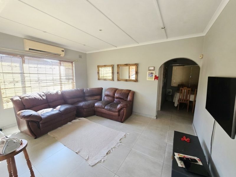 A comfortable living room featuring tiled flooring, a split-system air conditioner, and an arched entryway leading to the adjacent dining area.