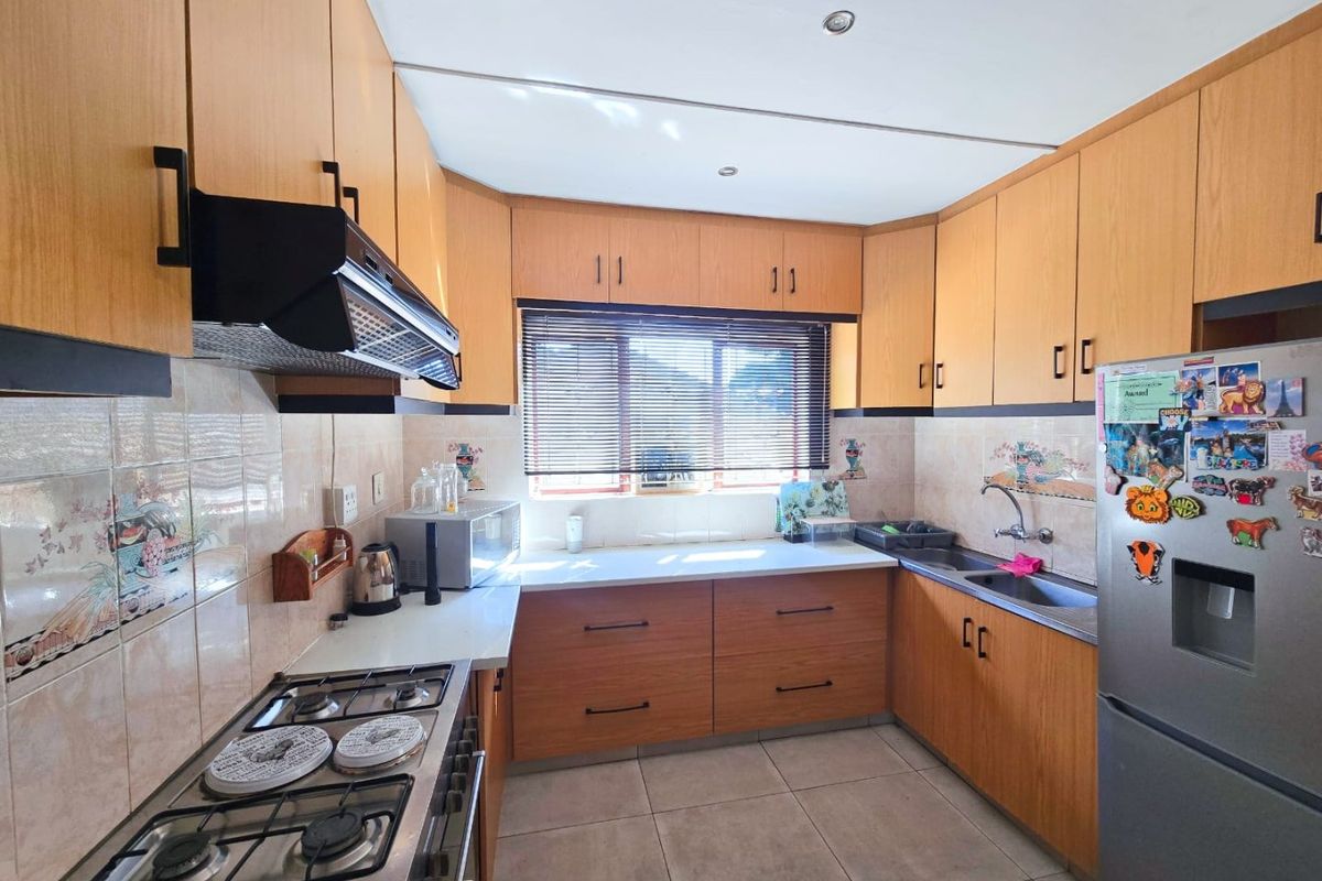 A functional kitchen featuring wood-finish cabinetry, a gas hob with extractor fan, tiled backsplash, and tiled flooring, offering a practical layout for daily cooking.