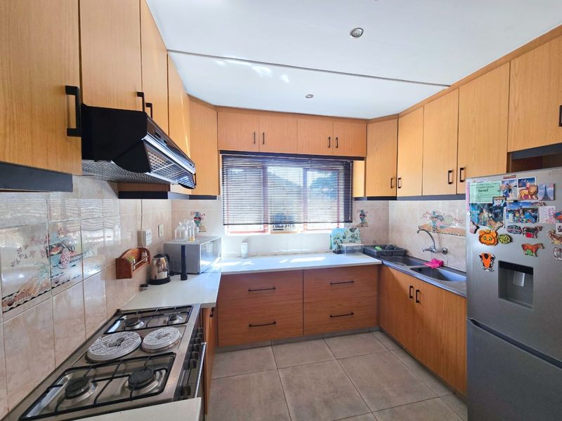 A functional kitchen featuring wood-finish cabinetry, a gas hob with extractor fan, tiled backsplash, and tiled flooring, offering a practical layout for daily cooking.
