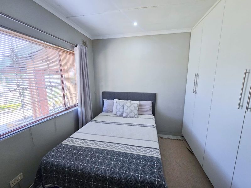 A functional bedroom featuring neutral walls, built-in white wardrobes, and venetian blinds, providing a clean and practical living space.