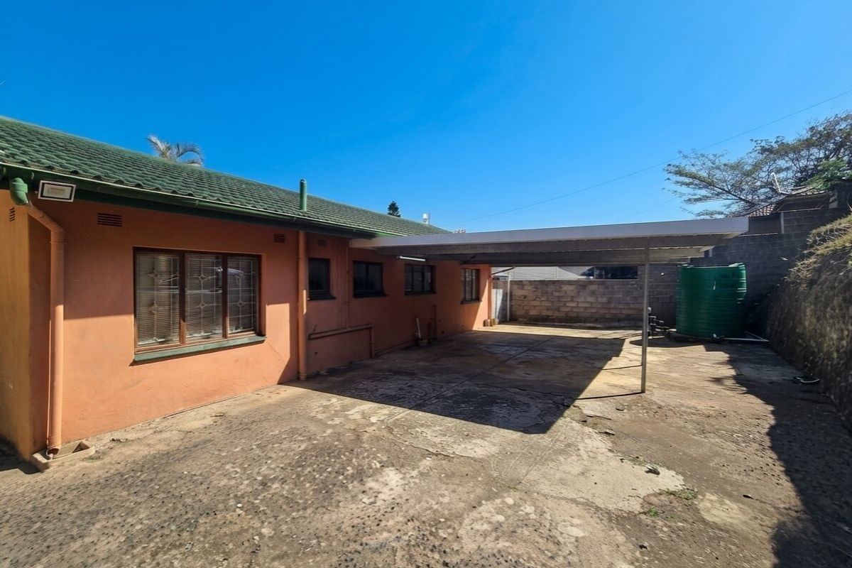 Rear exterior view featuring a concrete driveway, a covered carport, and a water storage tank against a brick boundary wall.