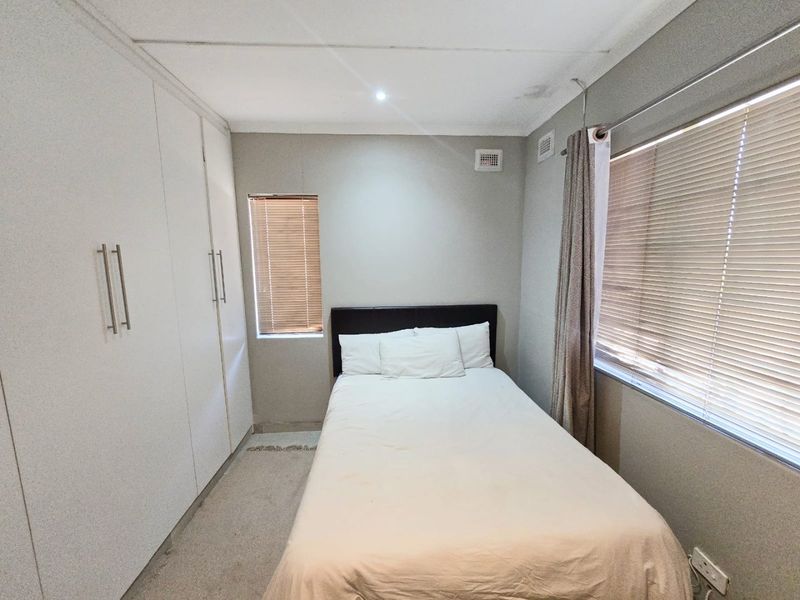 A functional bedroom featuring built-in cupboards, venetian blinds, and neutral finishes, providing a comfortable and practical living space.