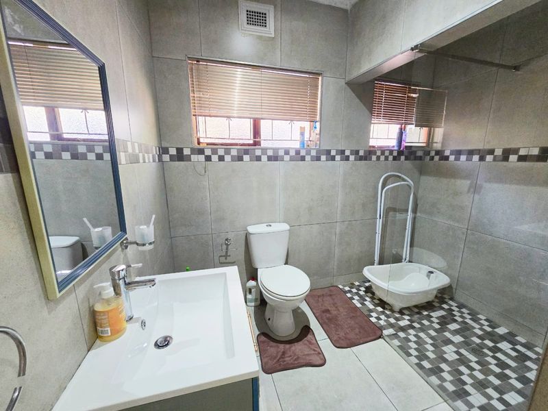 A modern tiled bathroom featuring a vanity basin, toilet, and a walk-in shower area with neutral finishes and good natural light.