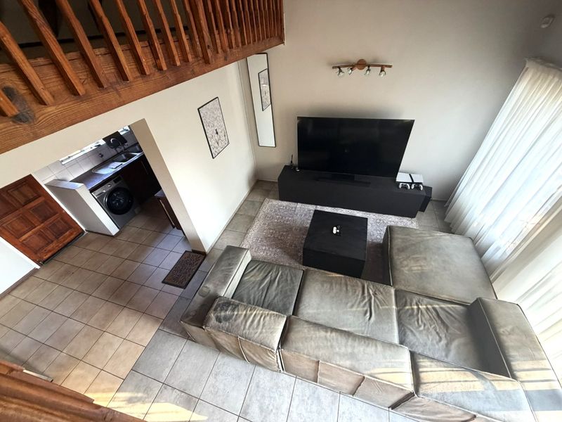 Open plan living area featuring tiled floors, a mezzanine level with wooden railing, and an adjacent kitchen and laundry area.