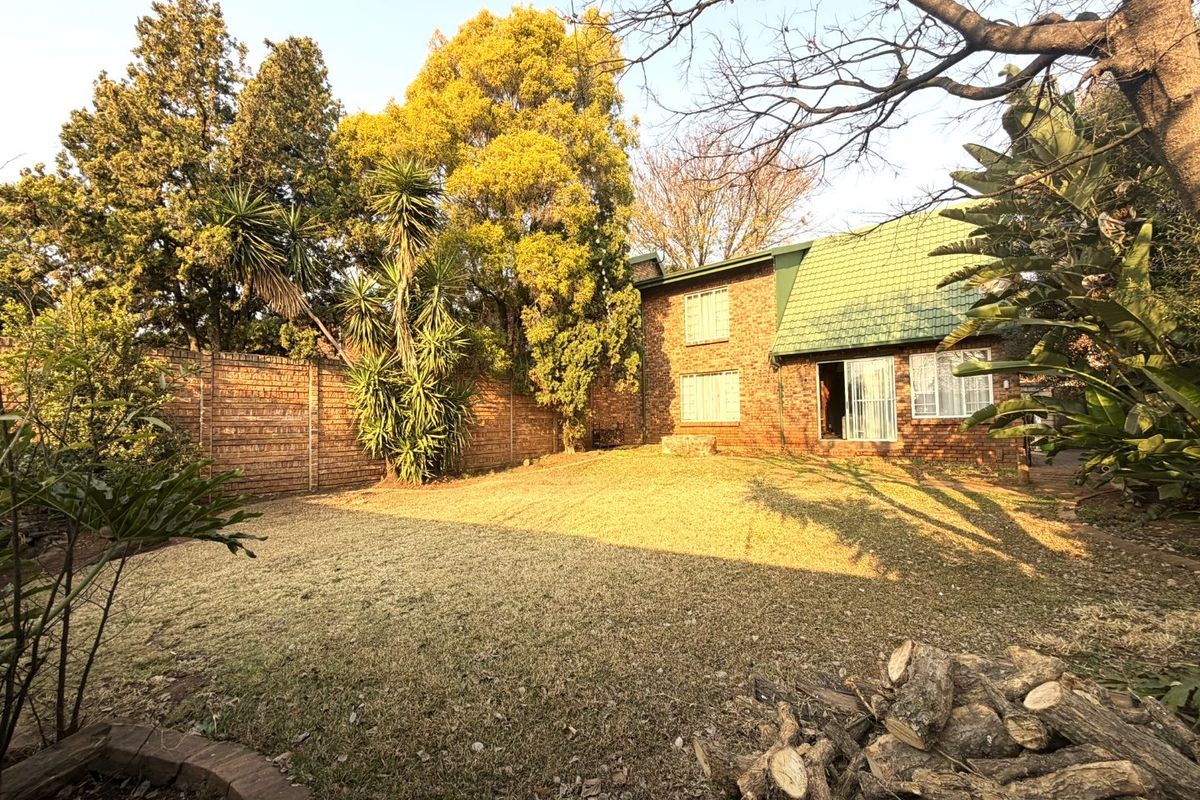 A rear view of the townhouse featuring a private garden, brick exterior walls, and a tiled roof with a sliding door entrance.