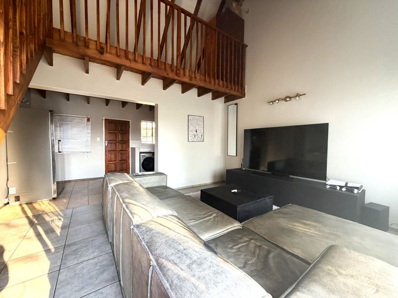 Open plan living area featuring high ceilings with exposed timber beams, a mezzanine level with wooden railing, and tiled flooring throughout.